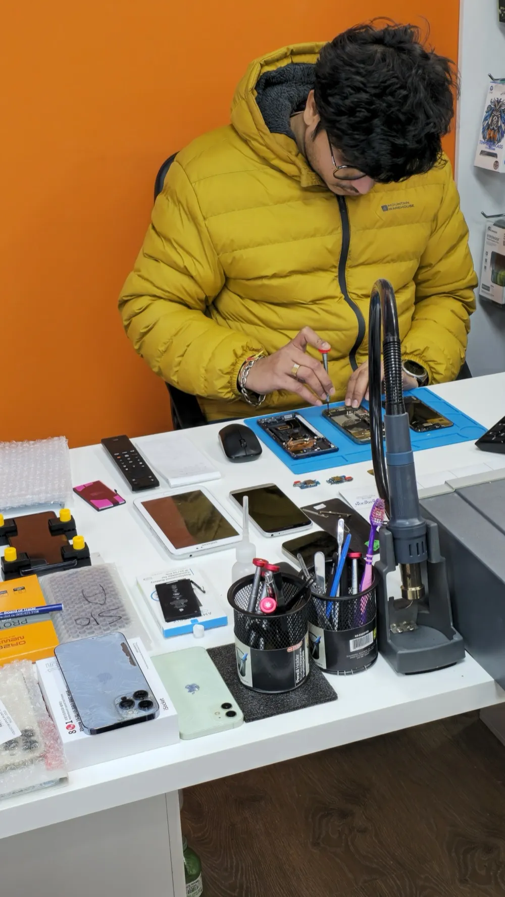 A Phone Studio technician repairing a phone at the workbench in Courtice, with a disassembled device, magnifier lamp and tools on the counter.